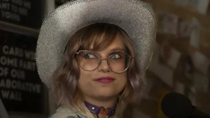 A woman in a sparkly cowboy hat and glasses stands in front of a microphone.
