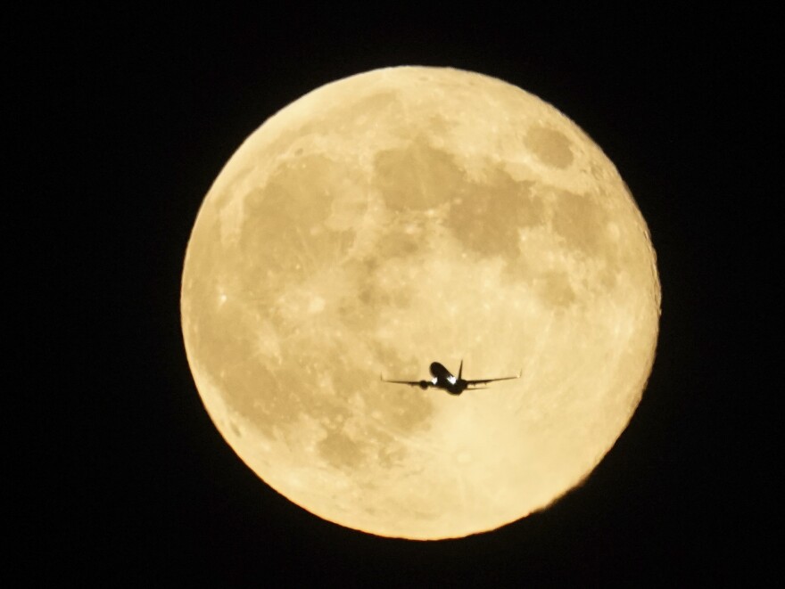 An airplane flies past the moon as it rises over Lake Michigan, Thursday, Oct. 17, 2024, in Chicago.