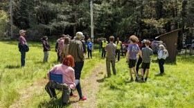 People sitting and standing in a park for a community meeting.