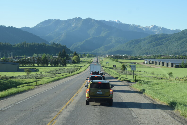 A row of cars on a road crossing through a green valley with mountains ahead.
