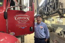 Smiling man in blue workshirt standing by big red red truck which on the door reads 'Giroux Body Shop, Hinesburg, Vermont' 