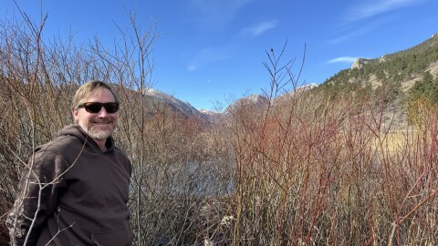 Jeremy Shaw stands in front of a beaver dam covered by willows.