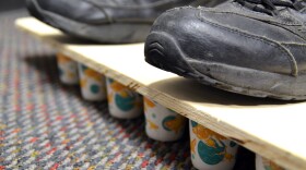A closeup photo of shoes standing on the board with many dixie cups below the board.