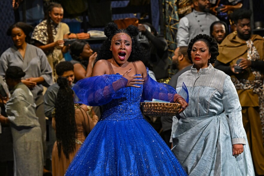 a woman in a blue dress stands on stage with her mouth open in song