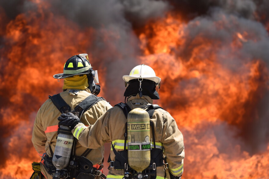 Two firefighters stand in front of a blaze