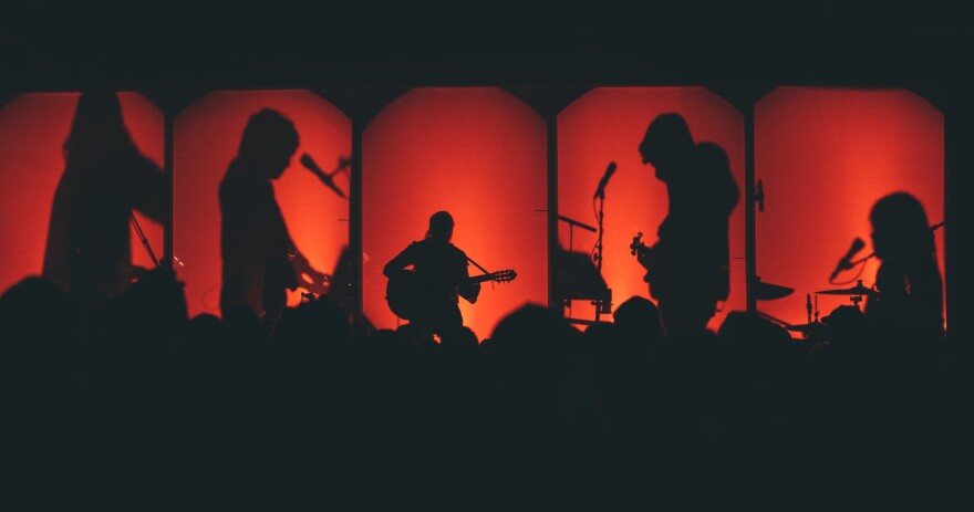 Five musicans perform on stage behind red screens so only their silhouettes are visible to the audience.