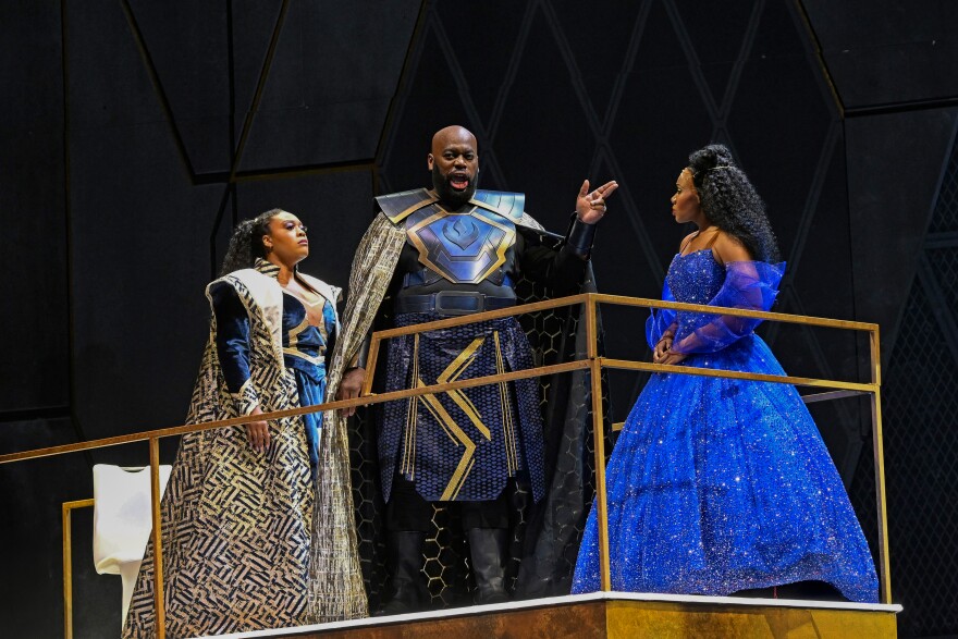 two women and one man stand on a stage in costume