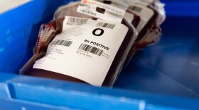 Bags of blood sit in a blue plastic container. The top one has a visible label that says O positive. 