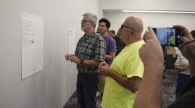 A small group looks at a big piece of paper with notes on it stuck to a wall