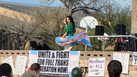Drag artist Yazmean La Patrona dances on stage with the trans flag for the Transgender Day of Visibility celebration in Tiguex Park.