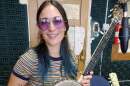 Cristina Vane holding her banjo, wearing purple sunglasses and a striped shirt.