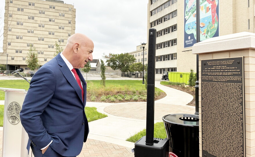 A man in a navy suit looking at a bronze plaque on a stand at Bradley University.