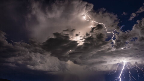 Lightning strikes the ground across a dark blue stormy sky