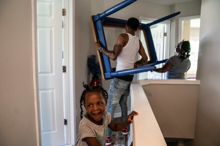 Tasharn's son Geoff Newman helps her move a table as her 5-year-old daughter, Khlema Richardson, smiles with excitement.