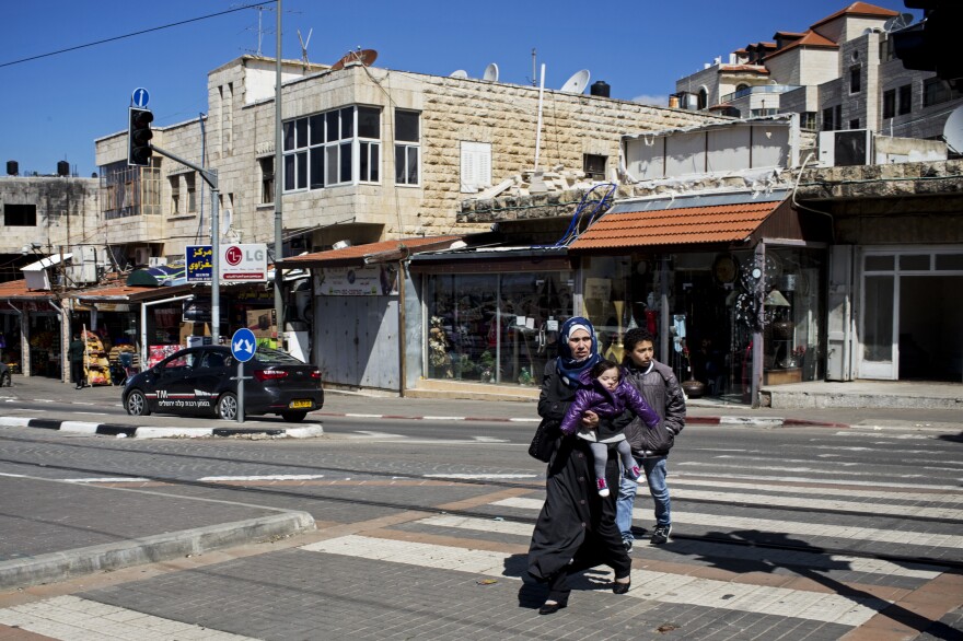 A Palestinian mother and her two children cross the light rail line in East Jerusalem. Nearby is a plaque dedicated to a 16-year-old Palestinian who was kidnapped at the spot and murdered by Israelis in a revenge killing.