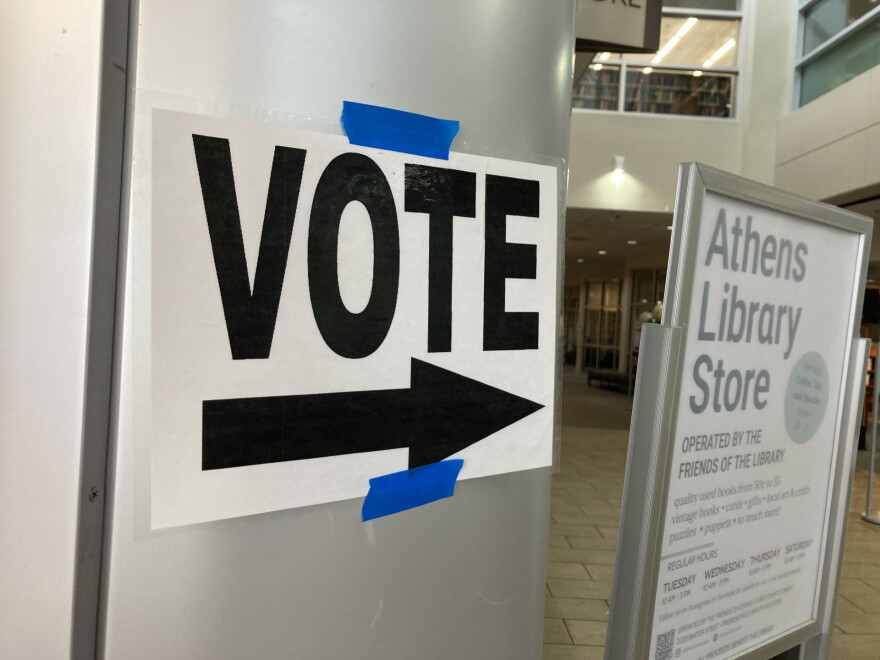 a white sign with "VOTE" and an arrow, printed boldly in black, pasted to a door, directing voter traffic at a library.