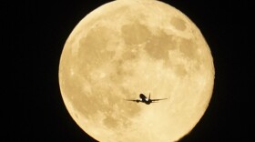 An airplane flies past the moon as it rises over Lake Michigan, Thursday, Oct. 17, 2024, in Chicago.