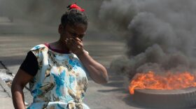 A woman walks past burning tires during a demonstration following the resignation of its Prime Minister Ariel Henry, in Port-au-Prince, Haiti.