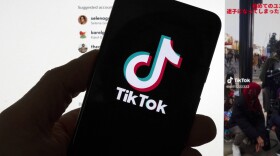The TikTok logo is seen on a mobile phone in front of a computer screen which displays the TikTok home screen. (Michael Dwyer/AP)