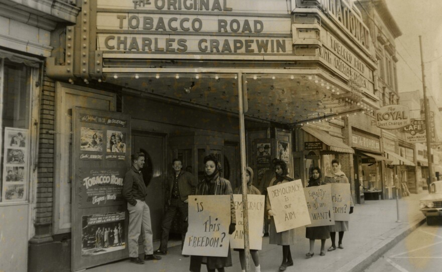 An archival, black and white photo of Black students protesting outside a movie theater.