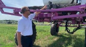 A man is standing next to a large purple sprayer. 