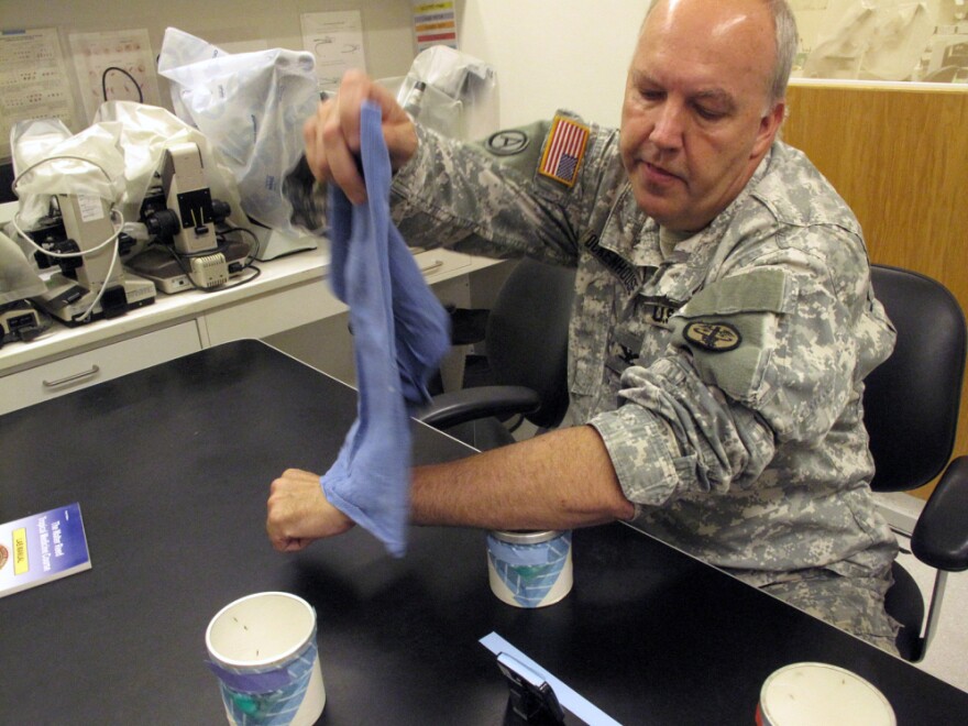 Col. Christian Ockenhouse, director of malaria vaccine research at Walter Reed Army Institute of Research, shows how volunteers are infected with malaria — by holding their forearms over a container holding five malaria-infected mosquitoes. The container is covered with a mesh, allowing the mosquitoes to bite the volunteers.