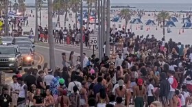 large group of people gathered on a beach sidewalk, water and sand in the background