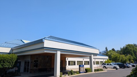 The entrance to a building with a blue metal roof. A sign in the distance reads, "Asante"