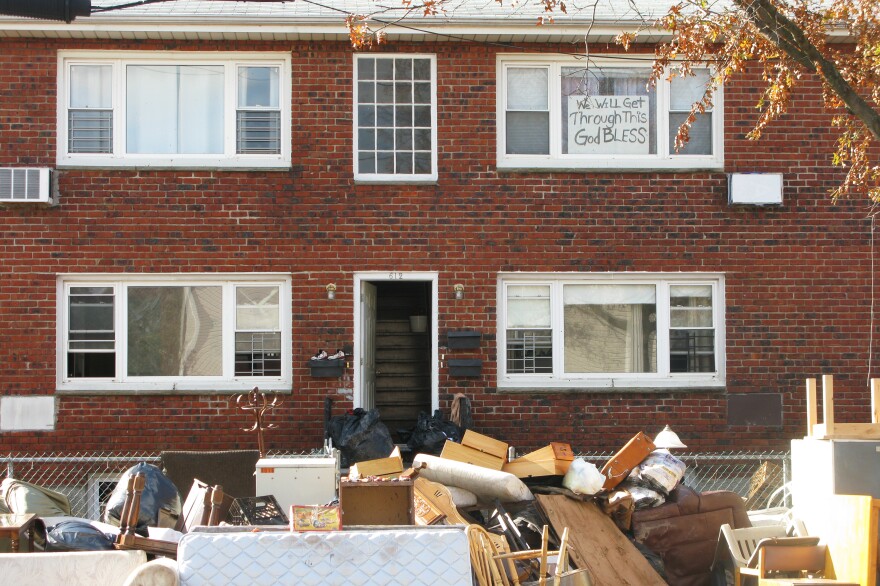 An apartment building's contents are placed on the sidewalk during cleanup from Superstorm Sandy. The sign in the window reads, "We will get through this. God bless."