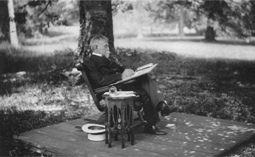 Black and white photograph of author and Civil War general Lew Wallace sitting in a rocking chair on a wooden platform outdoors, writing under a large beech tree.