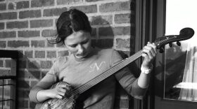 Nora Brown, seated in a chair, playing a four string banjo