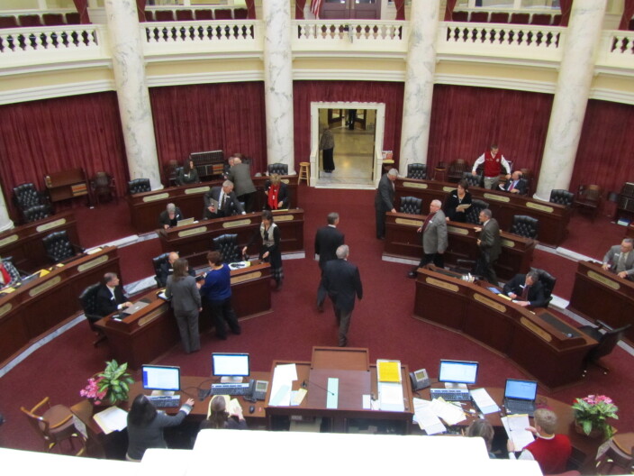 A view from the gallery of the Idaho Senate with senators standing around the room.