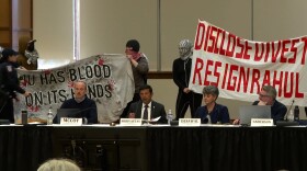 Protesters stand behind Provost Rahul Shrivastav and leader of the Bloomington Faculty Council meeting on March 25.