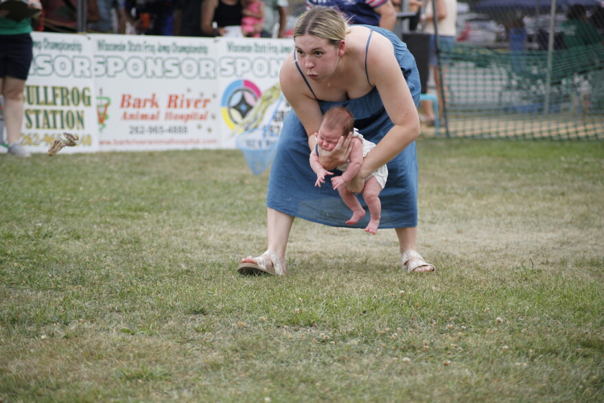 Ashlyn Hettich holding her one-month-old baby daughter, Emery Rose during the Wisconsin State Frog Jump. (credit: Dan Wanschura / Points North)