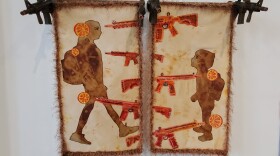 "Wounds the Size of Oranges" by artist Patricia Anderson Turner. "Emergency room doctors describe their horror and helplessness when addressing the immense damage done to our children by the bullets from an AR-15 semi-automatic weapon, damage that is impossible to treat successfully. First responders are unable to stem the rivers of blood, physicians are unable to repair the massive tissue and organ disintegration. The shooter does not even have to make the effort to aim, once his target is hit it is a virtual death sentence. As one ER doctor said “They had no fighting chance at life.” Diptych 36” x 42” x 15” mounted on toy guns. Silk soaked in tea, figures rusted with automotive brake pads, assault rifles artist dyed and commercial fabrics, heavily beaded, border crocheted yarns