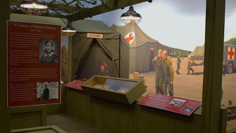 A wall mural of military nurses helping injured soldiers at a real evacuation hospital from WWII can be seen behind displays of Iowa nurses' stories and artifacts.