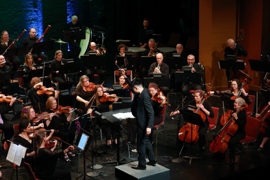 A conductor holds up his baton in front of a symphony orchestra