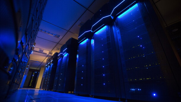 Rows of server banks glow blue inside an otherwise dark data center.