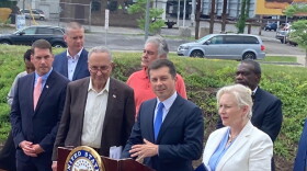 Secretary of Transportation Pete Buttigieg is flanked by New York's US Senators Chuck Schumer and Kirsten Gillibrand as he speaks outside the Syracuse Center of Excellence, with I-81 behind him.