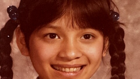 Older sepia photo of a young Asian girl with pigtails smiling at the camera