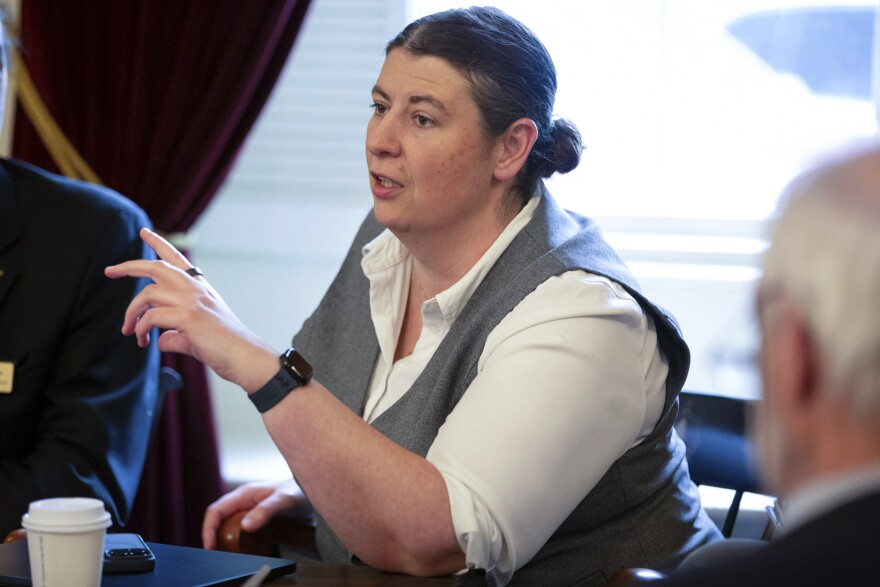 A woman sits at a table and gestures while speaking