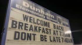 A sign outside Dunham Elementary School reading "Welcome Back! Breakfast at 7:15 AM, Don't Be Late 7:40 AM"