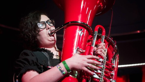 A woman in a green dress playing a red tuba