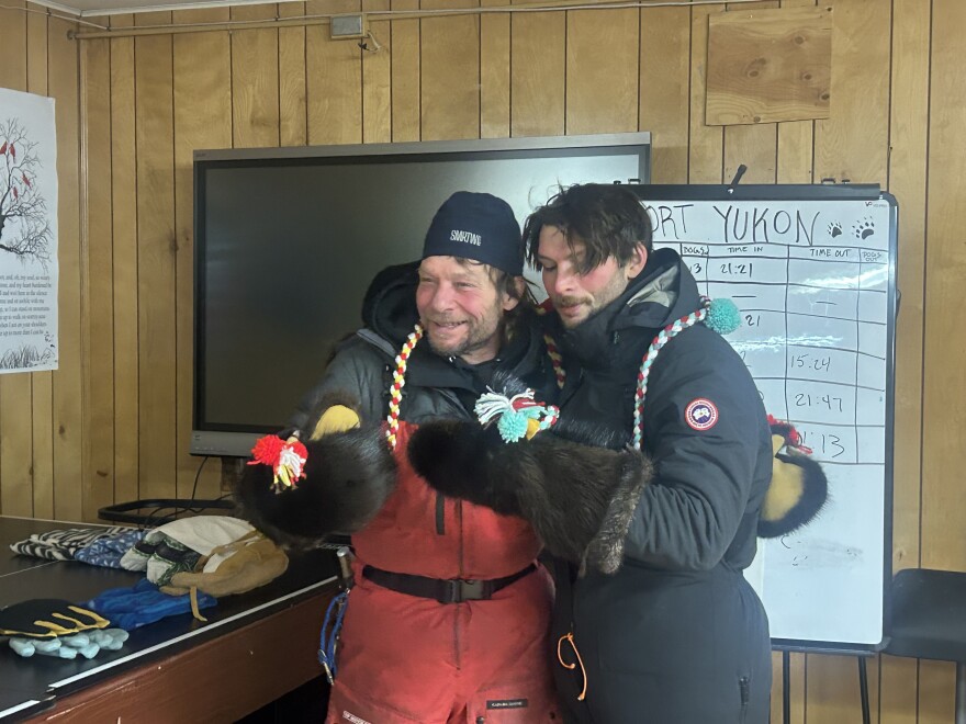Fresh off the trail, Jason Mackey (left) and Patrick Mackey (right) try on their new beaver mittens, which were gifted to them by Fort Yukon residents Corrima Cadzow and Louie Fairchild. (Shelby Herbert, KUAC)