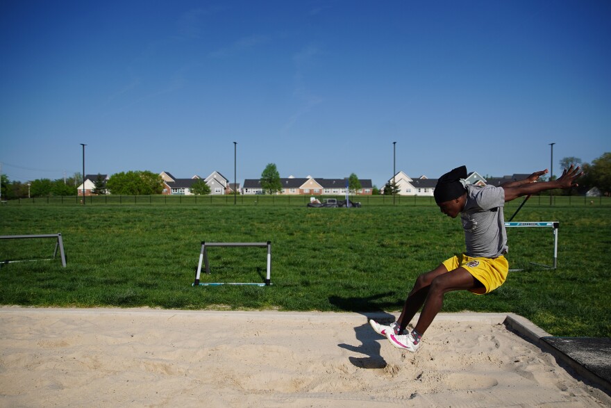 A boy in yellow shorts lands in the long jump sand box.