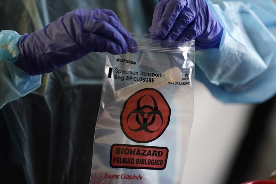 A health care worker deposits a vial containing a swab test into a bag at a mobile testing location for COVID-19, Tuesday, Dec. 8, 2020, in Auburn, Maine.