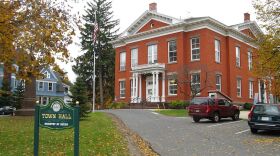 A brick building sits behind a green lawn.