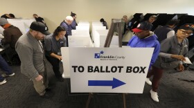 people mill about in a room filled with voting booths