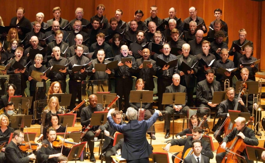 A man in a blue blazer conducts an orchestra