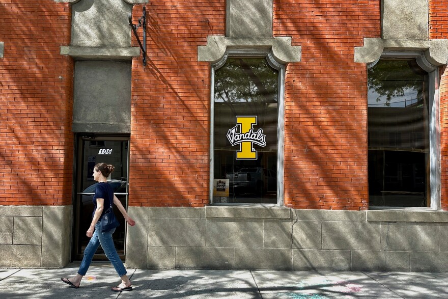 A person walks on a downtown street in Moscow, Idaho, in front of a building with a University of Idaho logo on a window on Tuesday, July 1, 2025. 